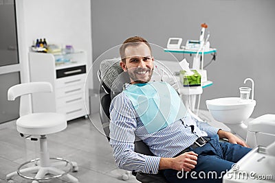 Man is smiling to the camera while sitting in a dental chair in dentistry being happy and satisfied with his treatment. Stock Photo