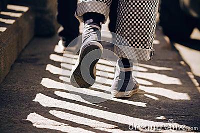 A man in sneakers and plaid pants walking on the pavement Stock Photo