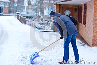 Man with snow shovel cleans sidewalks in winter during snowfall. Winter time in Europe. Young man in warm winter clothes Stock Photo