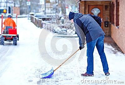 Man with snow shovel cleans sidewalks in winter during snowfall. Winter time in Europe. Young man in warm winter clothes Stock Photo