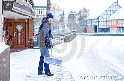 Man with snow shovel cleans sidewalks in winter during snowfall. Winter time in Europe. Young man in warm winter clothes Stock Photo