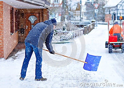 Man with snow shovel cleans sidewalks in winter during snowfall. Winter time in Europe. Young man in warm winter clothes Stock Photo