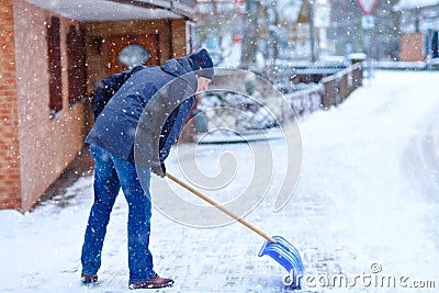 Man with snow shovel cleans sidewalks in winter during snowfall. Winter time in Europe. Young man in warm winter clothes Stock Photo