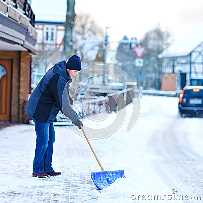 Man with snow shovel cleans sidewalks in winter during snowfall. Winter time in Europe. Young man in warm winter clothes Stock Photo