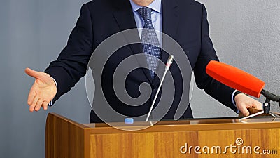 Man speaks in front of microphones, gesturing and standing behind a podium or pulpit. Lawyer, politician, businessman or teacher. Stock Photo