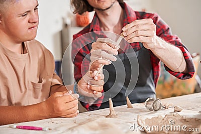 Man with special needs working with clay in ceramic studio under supervision of craftsman Stock Photo