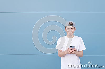 Man stand with a smartphone in his hands on a blue pastel background, listens music in the headphones Stock Photo