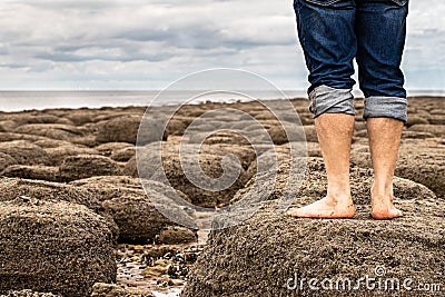 Man standing barefoot on the beach of stones on the seashore Stock Photo