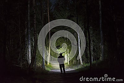 Man standing in dark forest at night with flashlight and hoodie on head Stock Photo