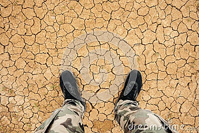 Man standing on a dry cracked earth. Feet in sneakers and in military pants standing on the cracked soil Stock Photo