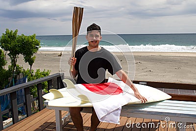 Man with Japanese flag , surfboard and torch used for sporting event. Stock Photo