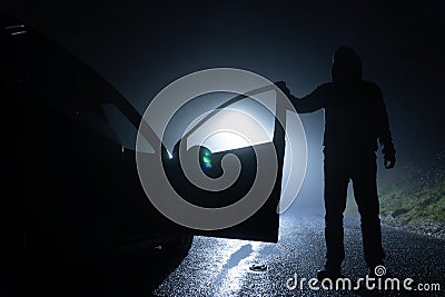 A man standing next to a car, with the door open, underneath a street light. On a foggy winters night Stock Photo