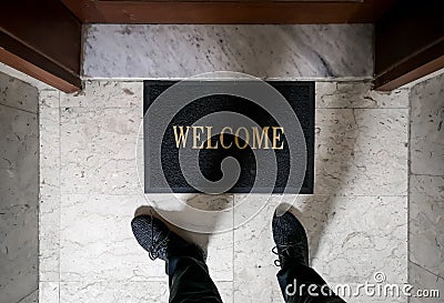 A man standing on top of a welcome floor mat in front of an apartment door Stock Photo