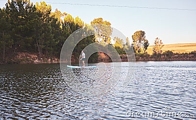 Man standing up on a paddle board on a quiet lake surrounded by trees in nature. Active man enjoying water sports on Stock Photo