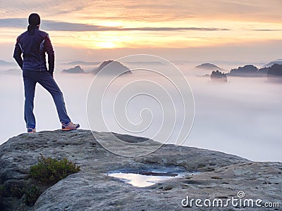 Man stands alone on the peak of rock. Hiker watching to autumn Sun at horizon Stock Photo