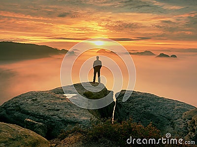 Man stands alone on the peak of rock. Hiker watching to autumn Sun at horizon . Beautiful moment the miracle of nature. Colorful Stock Photo