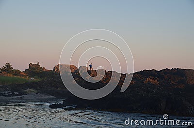 Man stands in fading light on rocky shore enjoying sunset from Spring Island Stock Photo