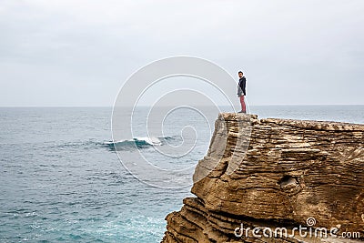 Man stands on a sea cliff, looking into the distance on a dark stormy sea. Stock Photo
