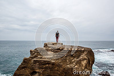 Man stands on a sea cliff, looking into the distance on a dark stormy sea. Stock Photo