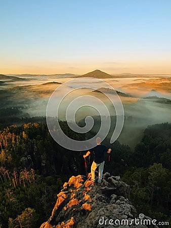 Man stay on the rocky peak and within daybreak watch over the misty and foggy morning valley. Beautiful autumn morning. Stock Photo