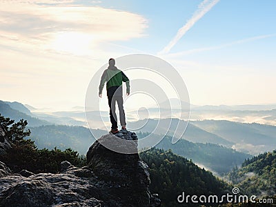 Man stay on rocky peak within daybreak and watch over misty landscape. Stock Photo