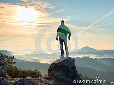 Man stay on rocky peak within daybreak and watch over misty landscape. Stock Photo