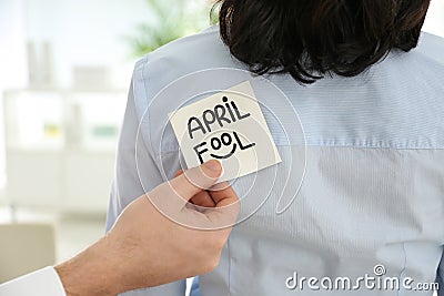 Man sticking APRIL FOOL note to colleague`s back in office Stock Photo