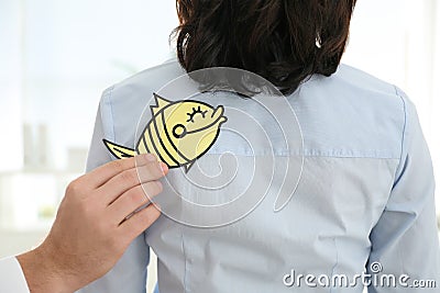Man sticking paper fish to colleague`s back, closeup. April fool`s day Stock Photo