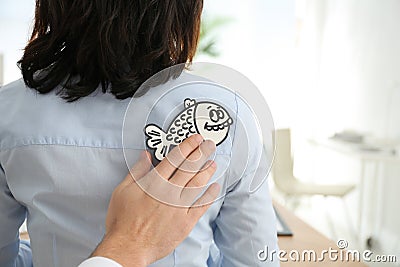 Man sticking paper fish to colleague`s back in office. April fool`s day Stock Photo