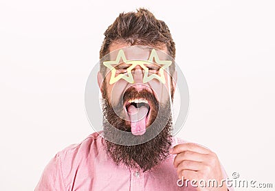 Man with stickout tongue, closed eyes and beard wearing paper star shaped glasses, fun concept. Hipster with crazy look Stock Photo