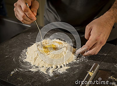 A a man stirring eggs into a mound of flour with a fork Stock Photo