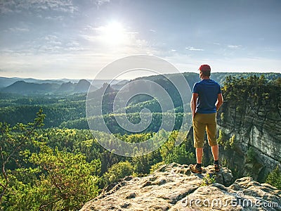 Man on stone observing the landscape. Lonely young sportsman stands on the mountain and looks into the far distance Stock Photo