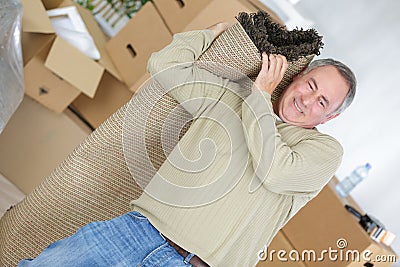 Man struggling to carry rug on shoulder Stock Photo