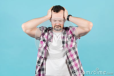 Man with stubble squeezes his head with his hands because of pain Stock Photo