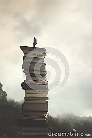 Man successfully reaches the peak of knowledge by climbing a stack of books Stock Photo