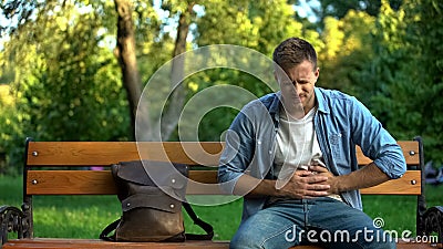 Man suffering stomach ache sitting bench, gastritis problem, food poisoning Stock Photo