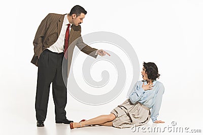 Man in suit pointing at seated woman on the floor, suggesting confrontation, dispute. Woman expressing shocked Stock Photo