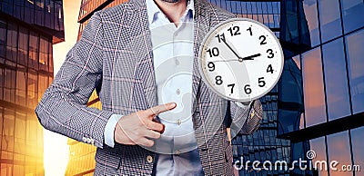 A man in a suit points to the clock on the background of a skyscraper Stock Photo