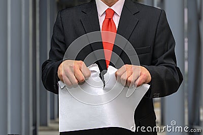 A man in a suit and tie tears up a sheet of paper against the background of metal structures. concept: terminate the contract, in Stock Photo