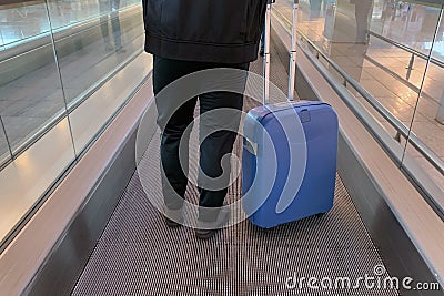 Man with a suitcase on wheels, photographed from behind, at the airport on a moving walkway Stock Photo