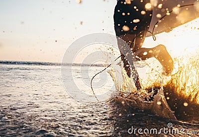 Man surfer run in ocean with surfboard. Closeup image water splashes and legs, sunset light Stock Photo