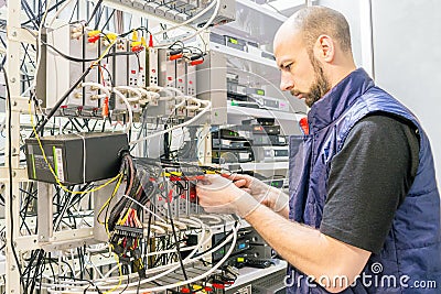 Man switches audio and video cable on the patch panel. Worker works on the control panel in the data center. Specialist connects Stock Photo