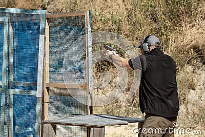 Man in tactical clothes shooting from a pistol, reloading the gun and aiming at the target in the open-door Shooting range. Stock Photo