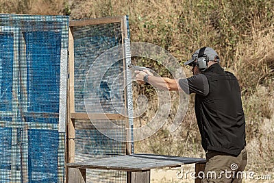 Man in tactical clothes shooting from a pistol, reloading the gun and aiming at the target in the open-door Shooting range. Stock Photo