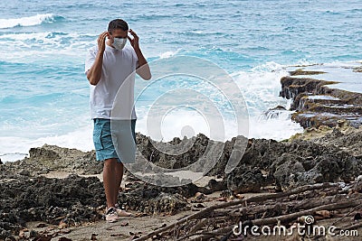 The man takes off/puts on a medical mask standing on the shore of the ocean. Stock Photo