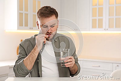 Man taking pill against migraine in kitchen, space for text Stock Photo