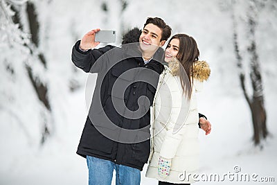 Man taking selfie photo young romantic couple smile snow forest outdoor winter pine woods. Couple make selfie. Stock Photo