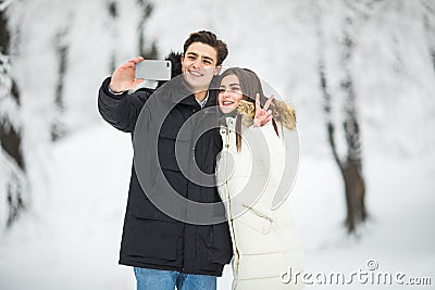 Man taking selfie photo young romantic couple smile snow forest outdoor winter pine woods. Couple make selfie. Stock Photo