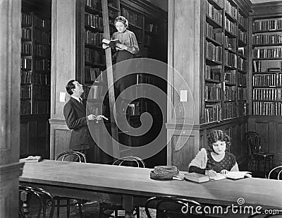 Man talking to a woman standing on a ladder in a library Stock Photo