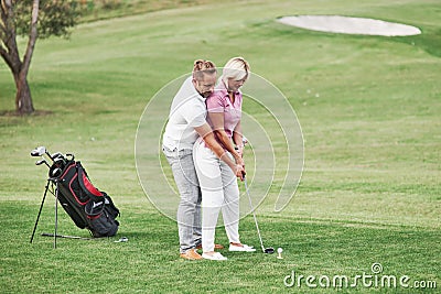 Man teaching woman to play golf at the sport field with equipment behind Stock Photo